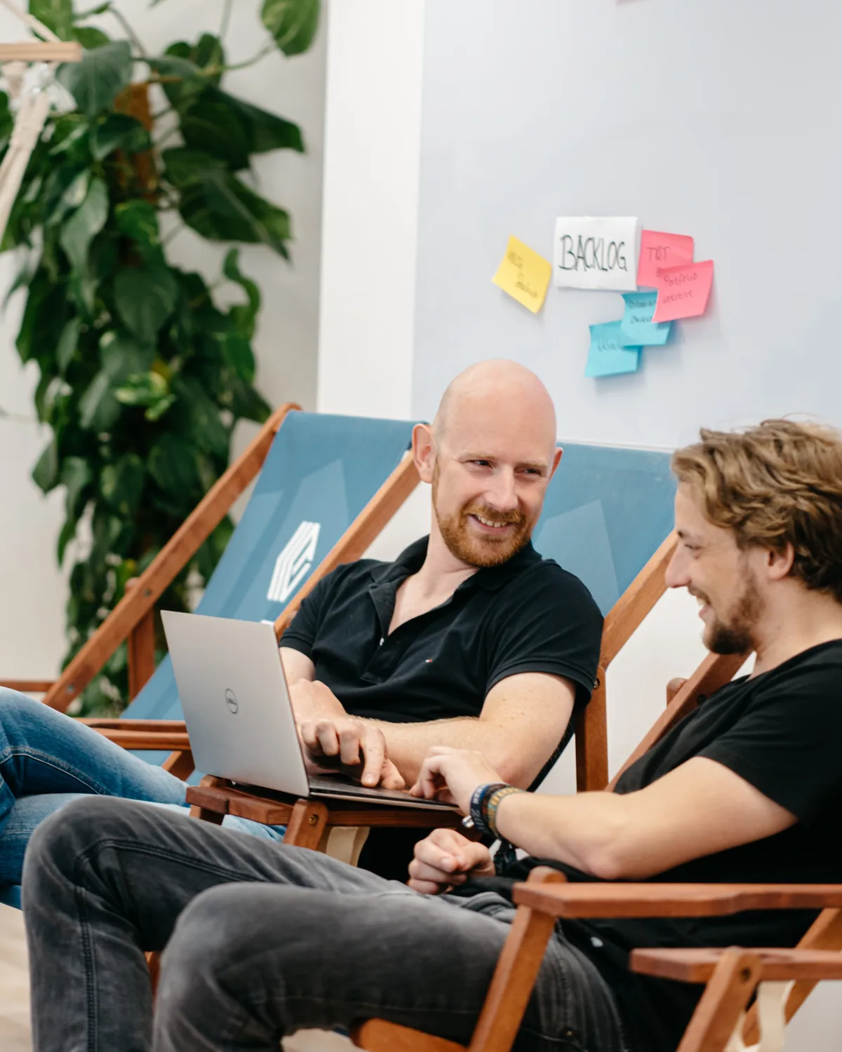 Entwickler arbeiten entspannt in Liegestühlen vor dem Backlog-Board